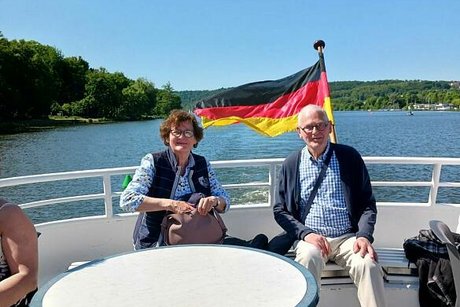 Eine Frau und ein Mann sitzen gemeinsam am Außendeck des Ausflugsschiffs. Im Hintergrund flattert eine Deutschlandfahne.