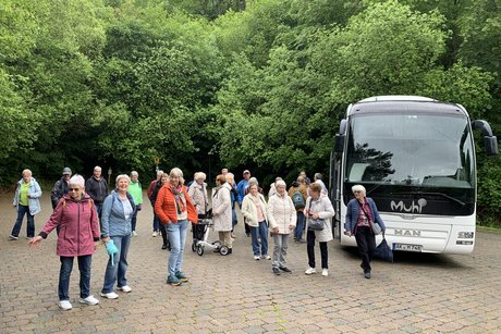 Parkplatz mit Bus, Menschen und B&auml;umen im Hintergrund