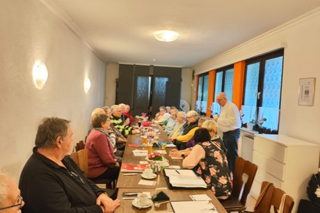 Mehrere Mitglieder des Ortsverband sitzen an einem langen Tisch und h&ouml;ren einem Mann zu, der einen Vortrag h&auml;lt.