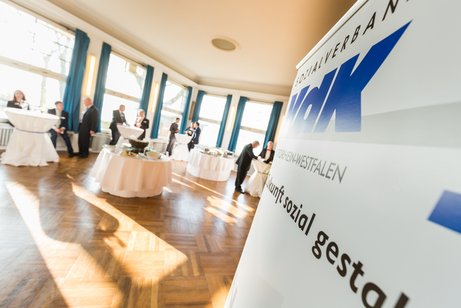 Saal mit wei&szlig; eingedeckten Tischen. Rechts im Bild ein Banner mit VdK-NRW-Logo und Slogan: Zukunft sozial gestalten.
