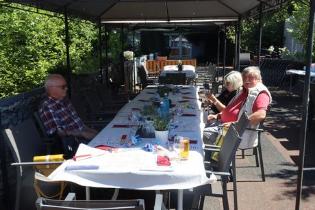 Drei Personen sitzen bereits an einem langen Tisch.