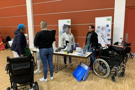 Das Bild zeigt an einem Messestand Beraterinnen und Interessierte vor mehreren Rollstühlen