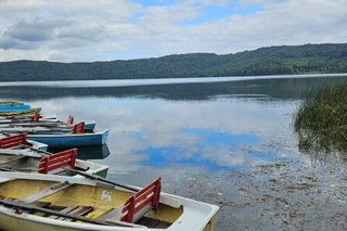 Panoramafoto eines Sees. Im Vordergrund liegen bunte Ruderboote an einem Holzsteg vertäut.