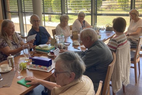Menschen sitzen an einem langen Tisch und unterhalten sich miteinander.