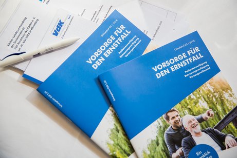 Zwei Broschüren und ein Stift und Block mit VdK-Logo liegen aufeinander gestapelt auf einem Tisch