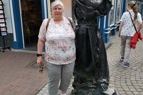 Ein eine Frau steht neben einer Figur aus Metall.