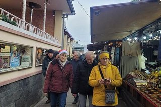 Eine Gruppe Menschen flanierte eine Gasse zwischen Hausfassaden und Weihnachtsmarktbuden entlang.