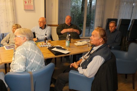 Mehrere Personen sitzen an einem Tisch und verfolgen einen Vortrag.