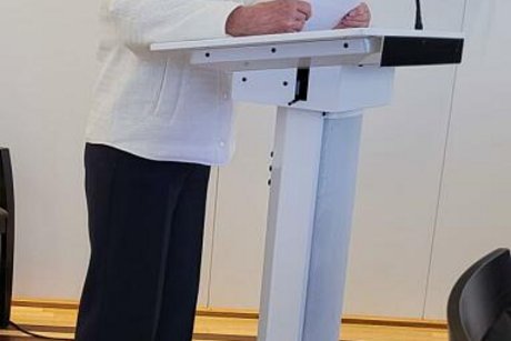 Eine Frau steht an einem Rednerpult und begrüßt die Gäste