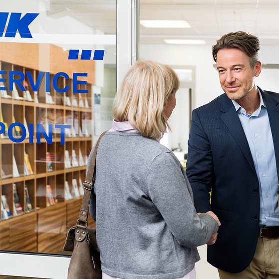 Ein VdK-Mitarbeiter begr&uuml;&szlig;t eine &auml;ltere Frau an der T&uuml;r einer VdK-Beratungsstelle. Er hat eine Aktenmappe unter dem Arm. 