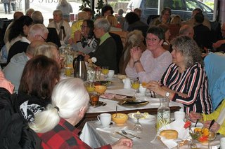 Viele Menschen sitzen gemeinsam beim Frühstück an einem langen Tisch.