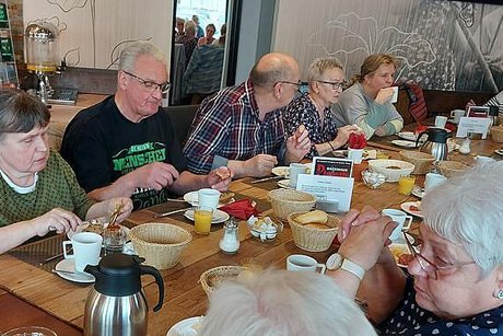 Viele Menschen sitzen gemeinsam beim Frühstück an einem langen Tisch.