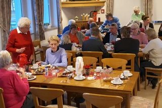 Viele Menschen sitzen an Tischen in einem Saal.