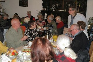 Viele Menschen sitzen gemeinsam beim Frühstück an einem langen Tisch.