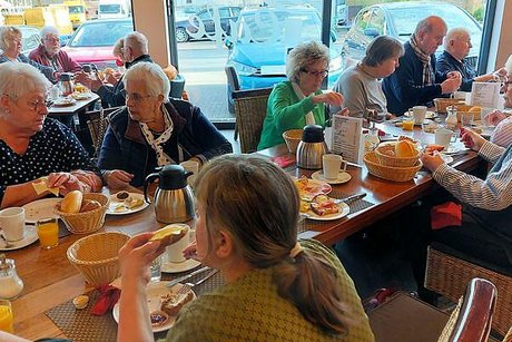 Viele Menschen sitzen gemeinsam bei einem geselligen Frühstück an einem langen Tisch.