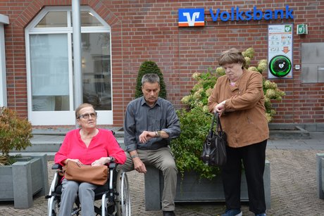 3 Personen schauen auf die Uhr und warten auf den Bus