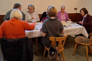 Sieben Menschen sitzen um einen Tisch herum bei Kaffee und Kuchen