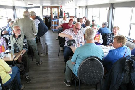 Menschen sitzen bei Getränken und Kuchen an Tischen des Ausflugschiffes.