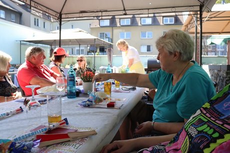 Menschen sitzen an einem langen Tischen im Au&szlig;enbereich.