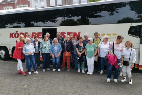 Viele Menschen stehen vor einem Reisebus für ein Gruppenfoto zusammen.