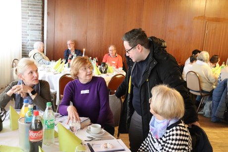 Drei Frauen sitzen am Tisch und unterhalten sich mit einem stehenden Mann.