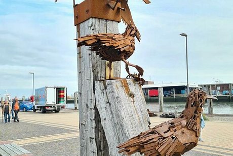 Vier Möwenskulpturen aus rostigem Stahl sind auf einem Poller in verschiedenen Posen arrangiert