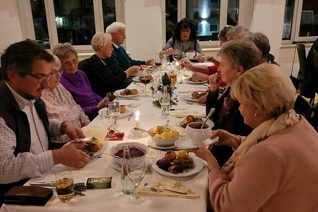 Menschen sitzen gemeinsam an einem langen Tisch beim Essen.