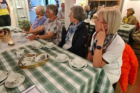 Menschen sitzen an einem Tisch zwischen Ausstellungsstücken des Teemuseums und trinken Tee aus dünnen Porzellantassen.