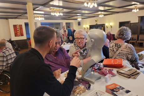 Hörtest 2 Mitglieder stehen am Pult um am Hörtest teilzunehmen. Ein mitarbeiter erklärt die Funktion.