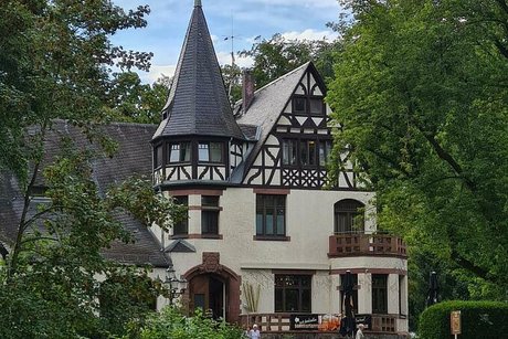 Fachwerkhaus mit Giebelturm umgeben von vielen Bäumen.