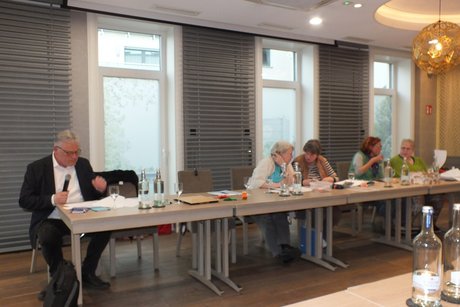 Ein Mann und drei Frauen sitzen an einem langen Tisch vor ihren Unterlagen.