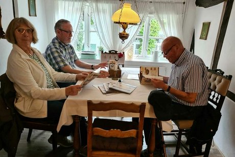 Zwei Männer und eine Frau sitzen am Tisch der Gaststube und blättern in der Speisekarte.