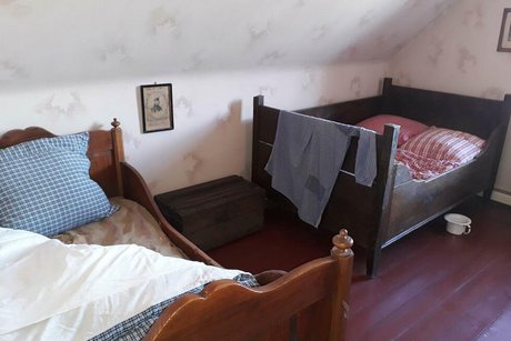 Blick in ein Giebelzimmer mit zwei altmodischen, kurzen Holzbetten.