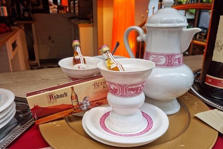 Stilleben abfotografiert: Eine Porzellankanne und Kaffeegedeck mit Rüdesheimer Schnapsfläschchen auf einem goldenen Tablett.