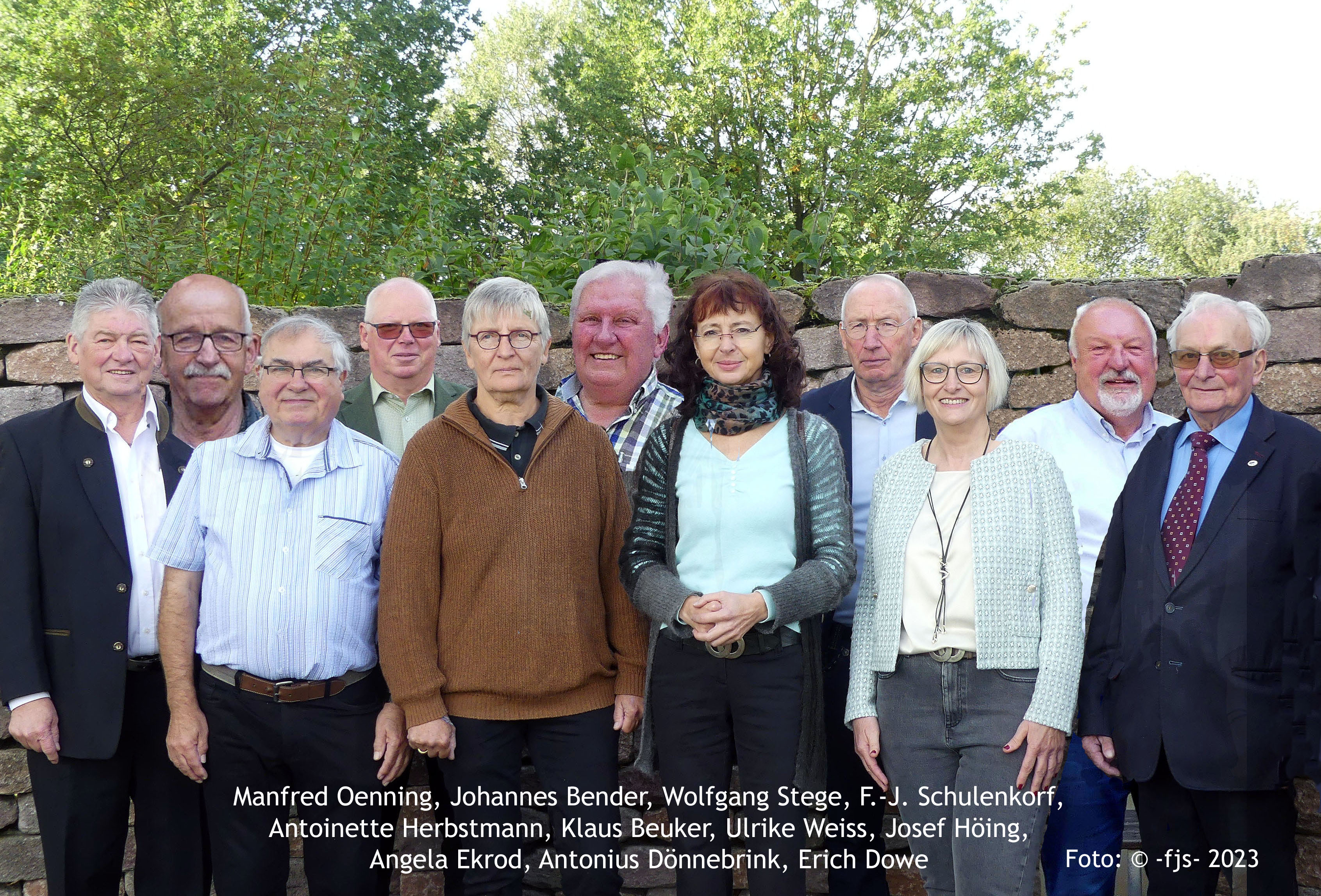 11 Personen stehen vor einer Mauer