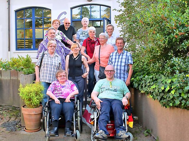 12 Menschen, zwei davon im Rollstuhl sitzend, haben sich für ein Gruppenbild aufgestellt