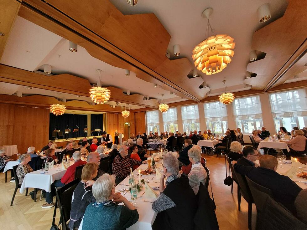 Menschen sitzen gemeinsam an langen Tischen in einem Saal.