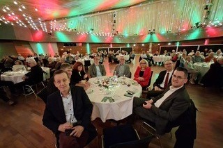 Menschen sitzen in einer festliche geschm&uuml;ckten Halle an Tischen.