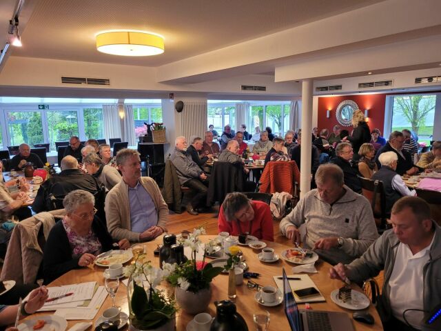 Viele Menschen sitzen an Tischen in einem Saal und essen.