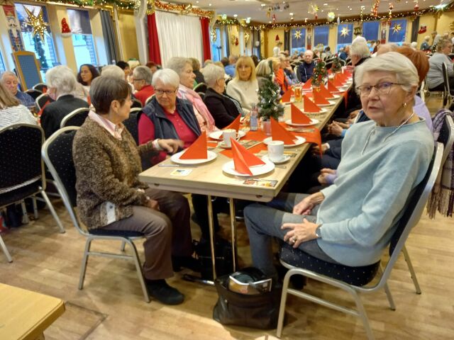 Viele Menschen sitzen an weihnachtlich geschmückten Tischen in einem Saal