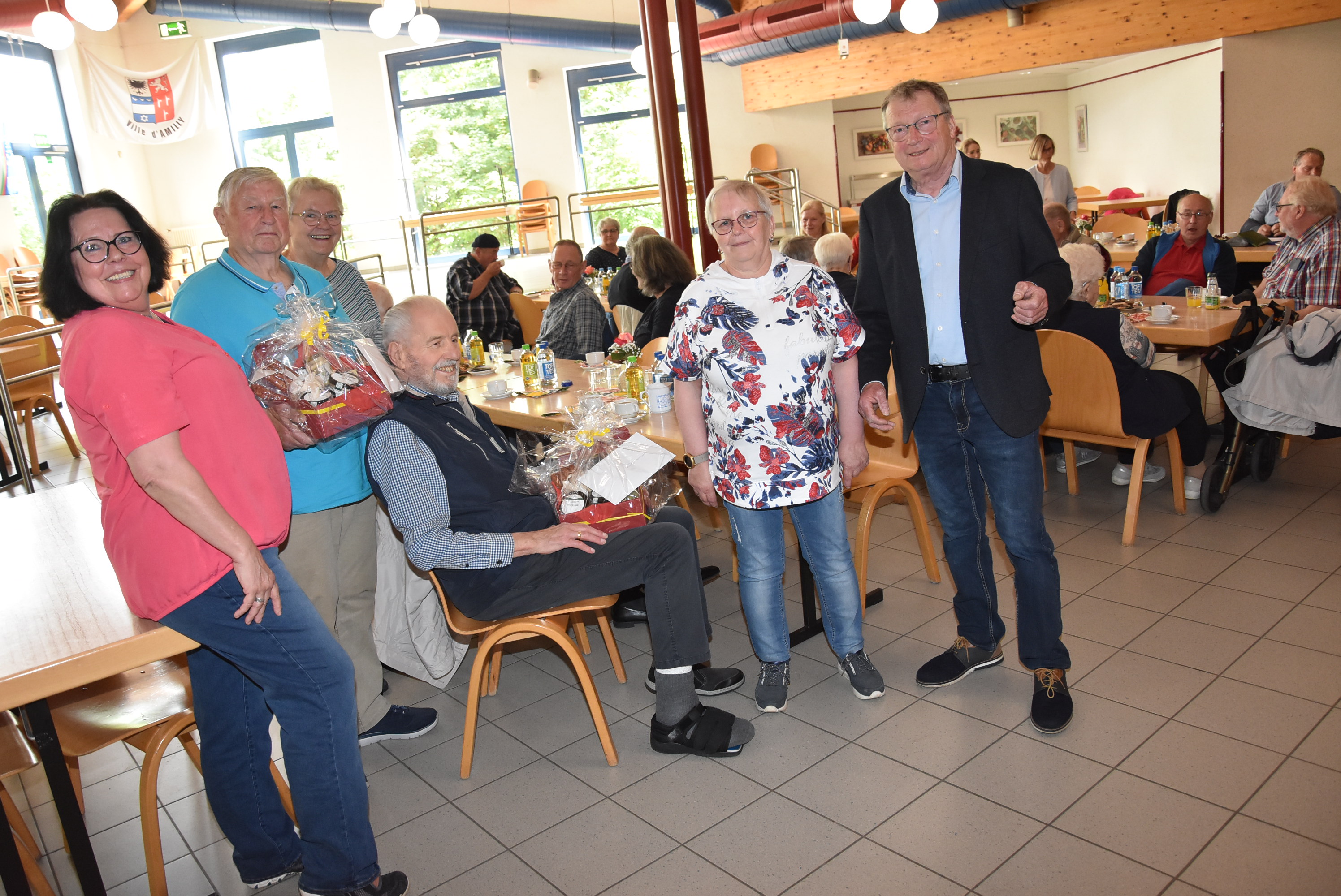 Gruppenfoto der Jubilare mit Präsentkörben. Im Hintergrund sitzen weitere Mitglieder des Ortsverbandes an Tischen.