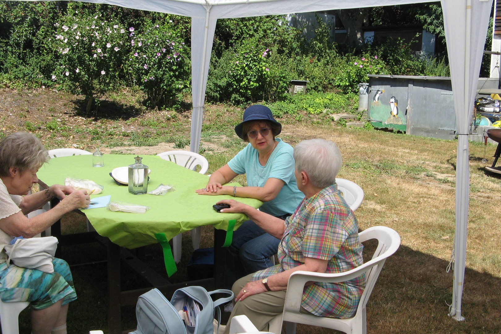 Grillnachmittag. Drei Personen sitzen an einem Gartentisch und unterhalten sich.