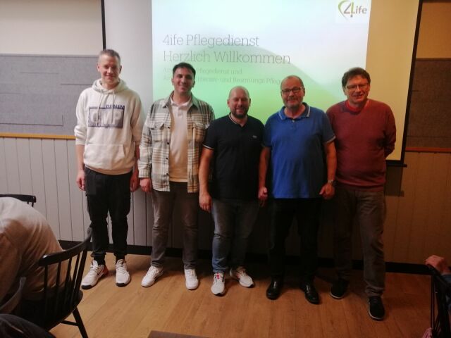 Gruppenfoto der Mitarbeiter des Pflegediensts 4life vor einer Leinwand mit Beamer-Präsentation