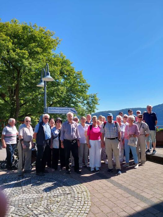 Die Reisegruppe hat sich auf einem Platz vor einem großen Baum und strahlendblauem Himmel aufgestellt.