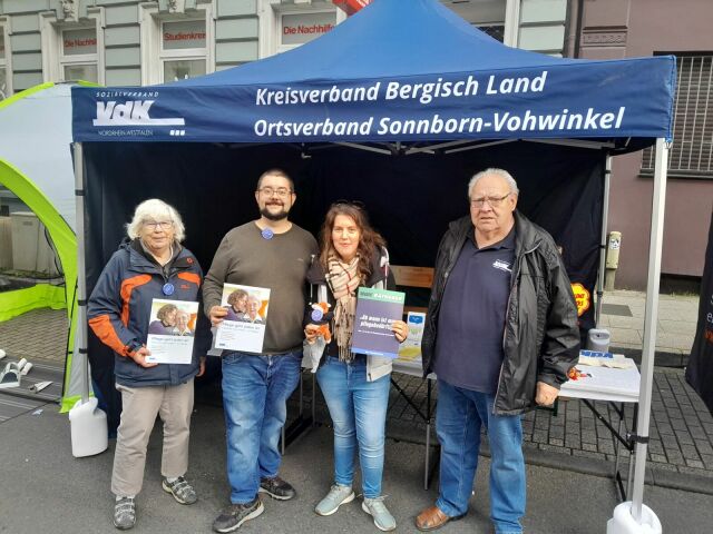 Zwei Frauen und zwei Männer stehen vor einem Pavillon des VdK Sonnborn-Vohwinkel und halten Broschüren in die Kamera.