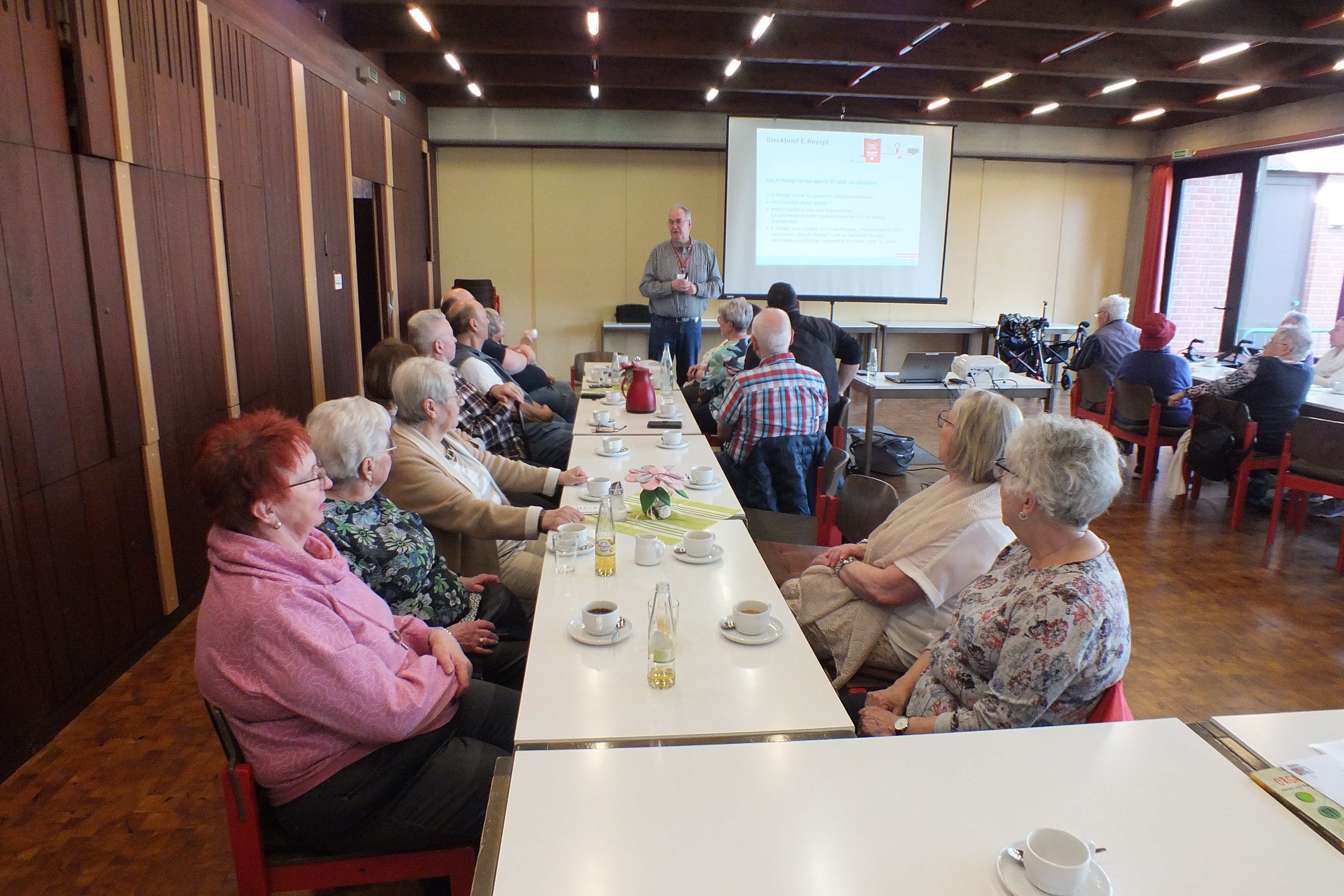 Ein Mann steht vor einer Leinwand und h&auml;lt einen Vortrag vor einer Gruppe.