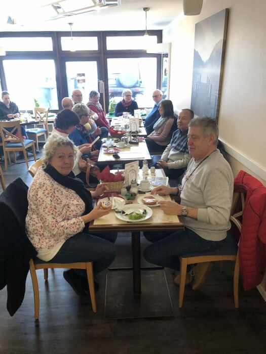 Männer und Frauen sitzen gemeinsam an einer langen Osterfrühstücks-Tafel im Stadtcafé