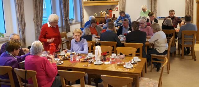 Viele Menschen sitzen an Tischen in einem Saal.