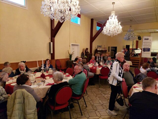 Viele Menschen sitzen an festlich eingedeckten Tischen in einem Saal.