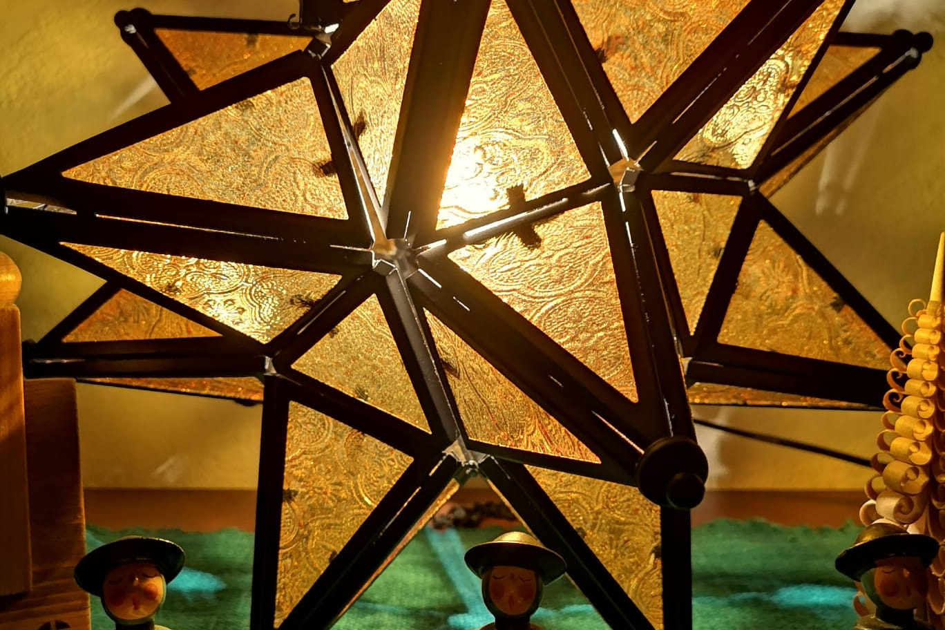 Zu sehen ist ein Herrenhuter Stern aus Metall und Glas in gelb und im Vordergrund ein paar Kurrendesänger aus Holz